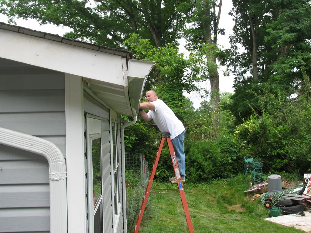 Man on a ladder cleaning out gutters